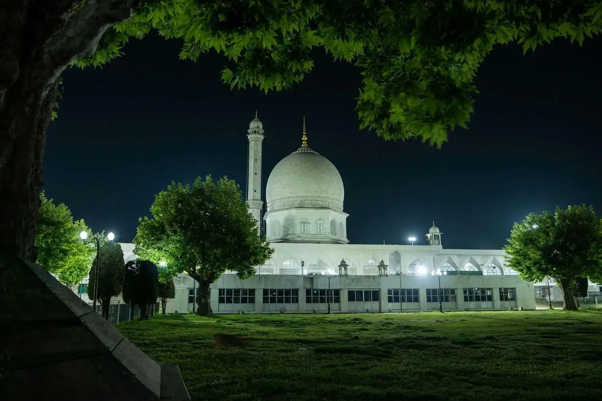 Night view of the illuminated Hazratbal Mosque surrounded by lush trees in Srinagar.