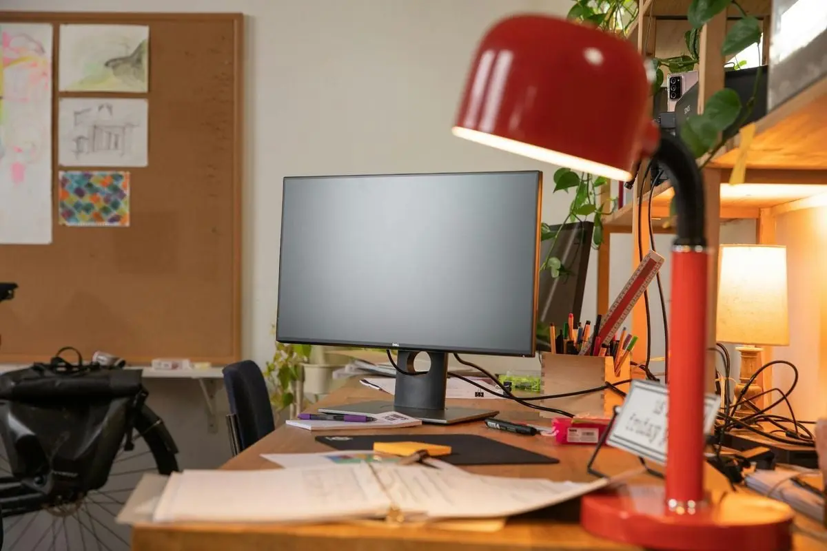 A cozy office workspace featuring a desktop monitor, red desk lamp, and various office supplies.