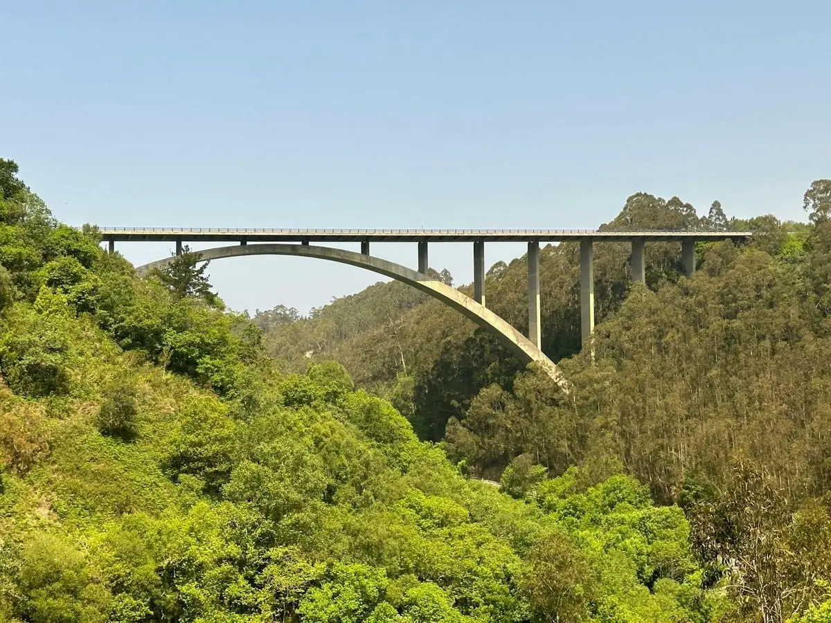 A scenic viaduct spans lush green valleys in Ballota, Spain, under a clear summer sky.