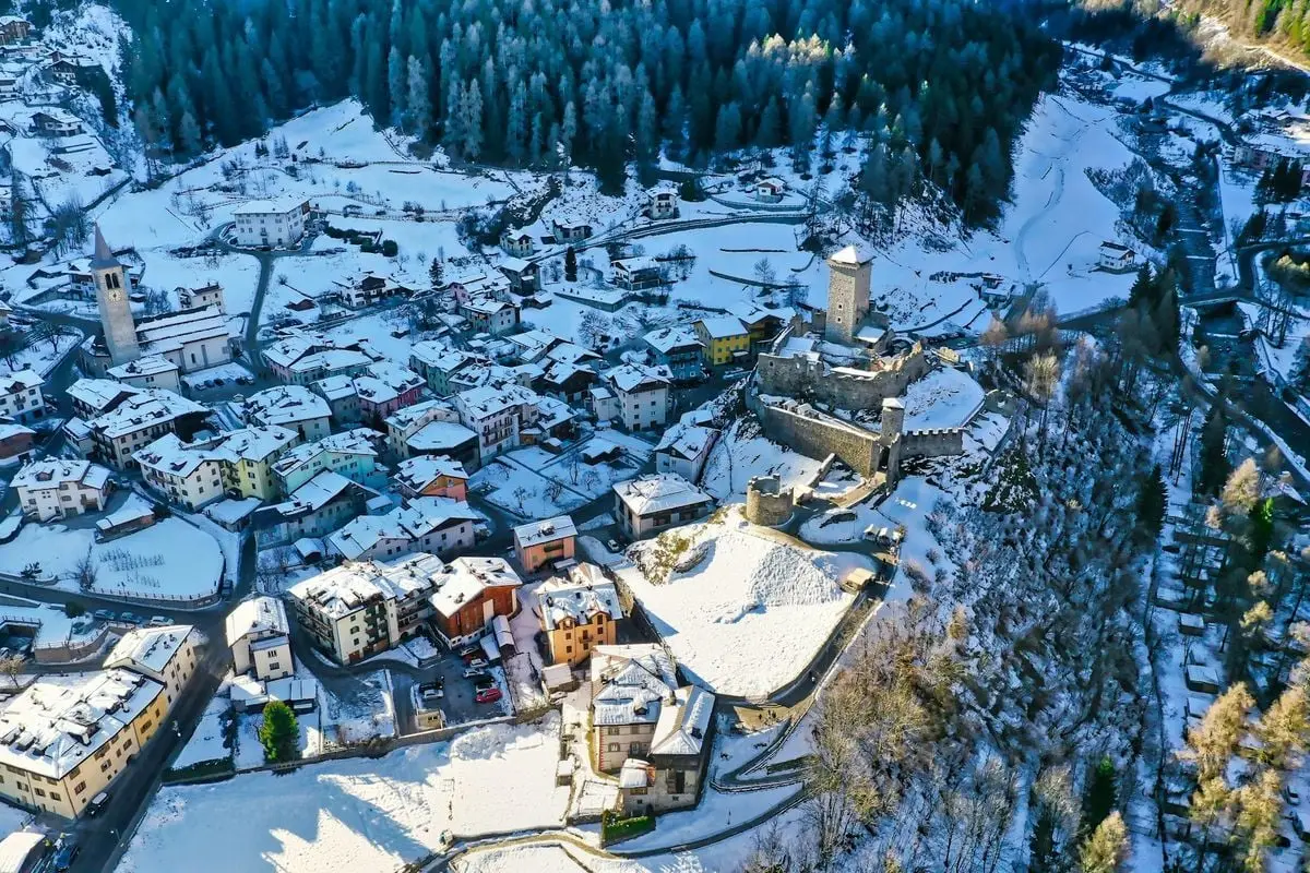 Aerial winter view of Pellizzano, Trentino-Alto Adige, showcasing snow-covered buildings and landscapes.