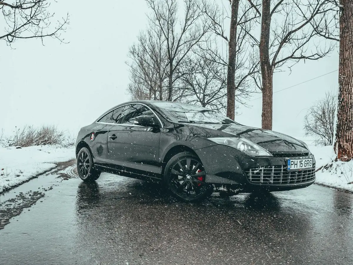 Sleek black car parked on a snow-covered road in Romania during winter, reflecting its elegant design.