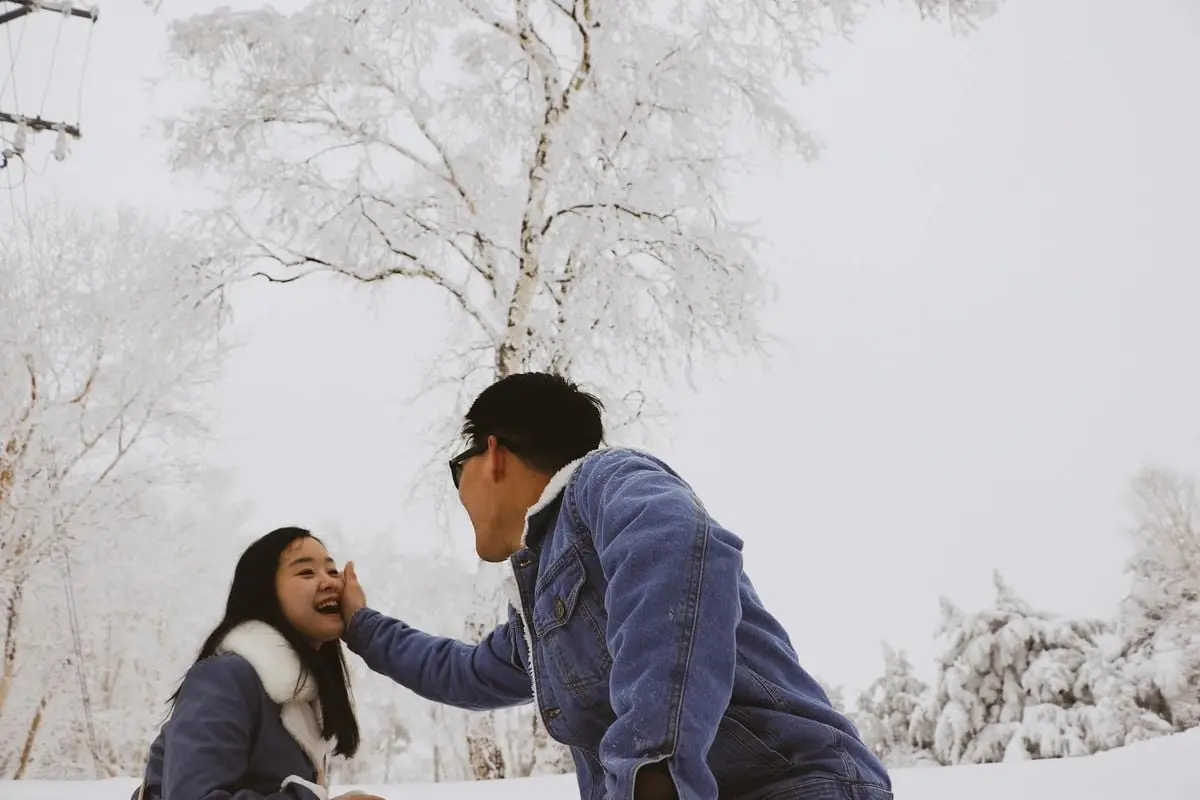 Asian couple enjoying a playful moment outdoors in a snowy winter park.