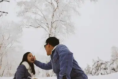 Asian couple enjoying a playful moment outdoors in a snowy winter park.