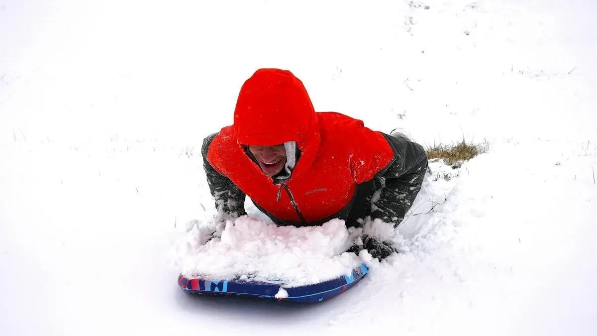 Adult enjoying winter sledding on snowy hill in vibrant red jacket.