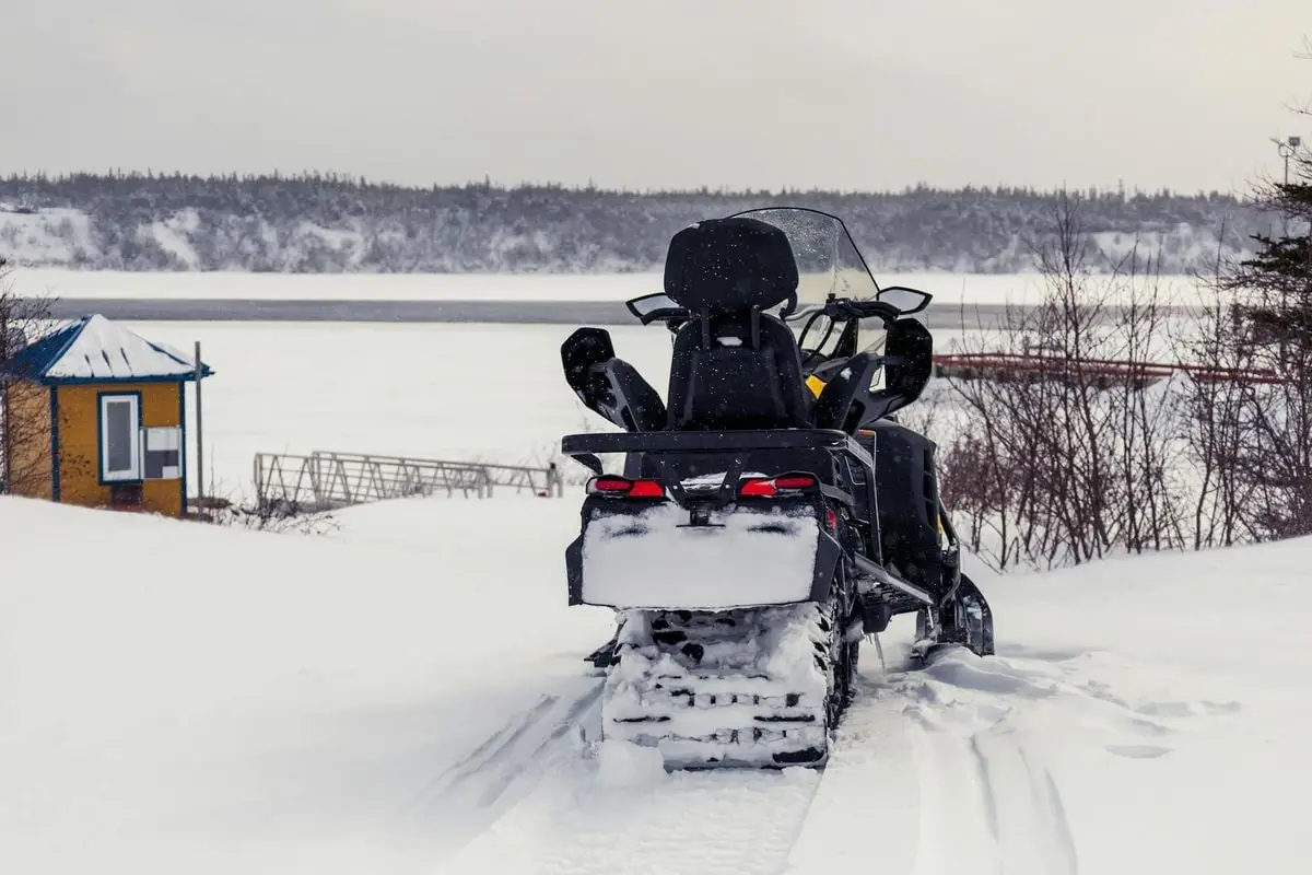 Explore the snowy landscape of Chevery, Québec with a snowmobile by the frozen lake.