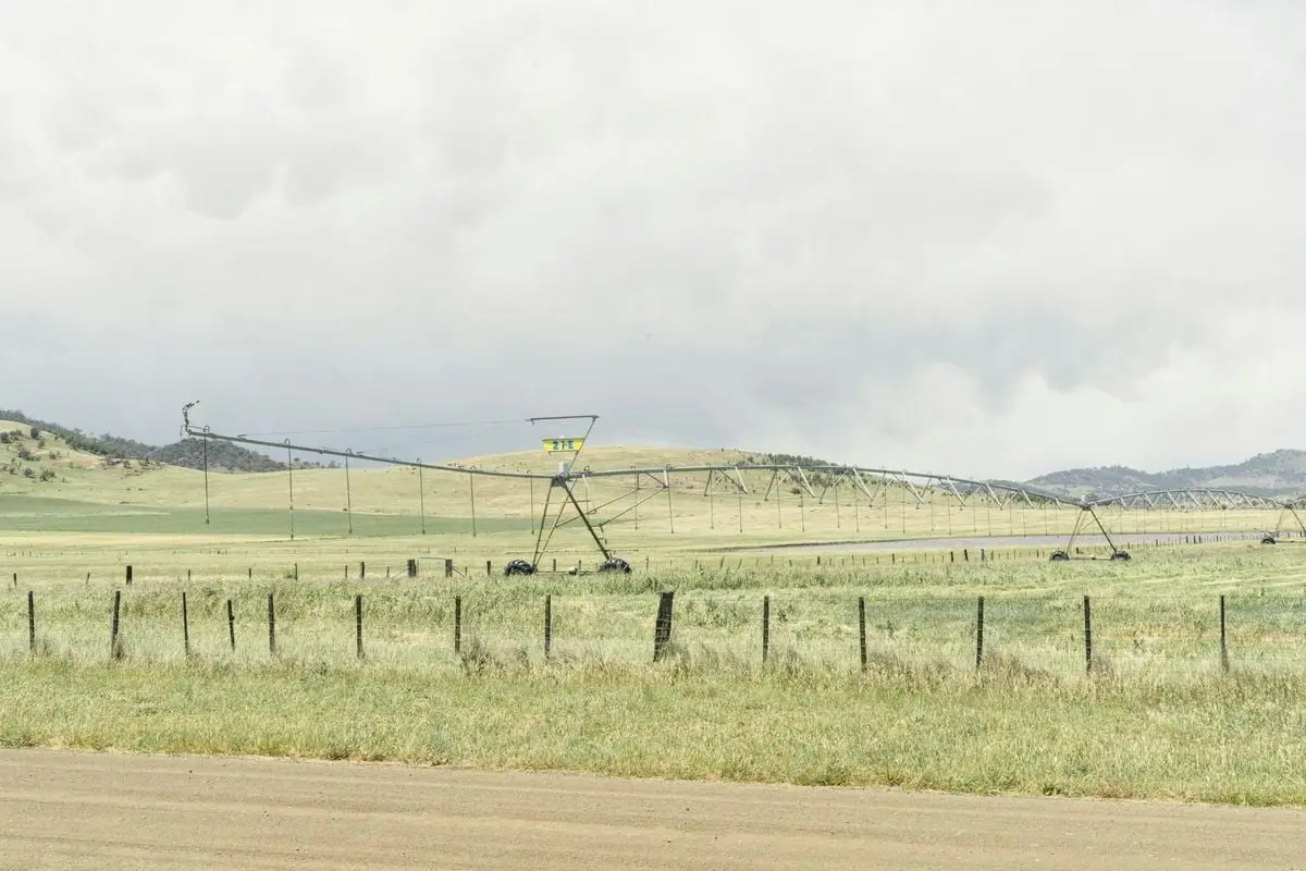 Wide view of an irrigation system in a rural green field landscape under a cloudy sky.