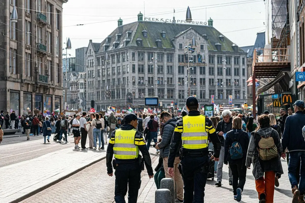 A bustling European street with police officers and diverse crowd under a sunny sky.