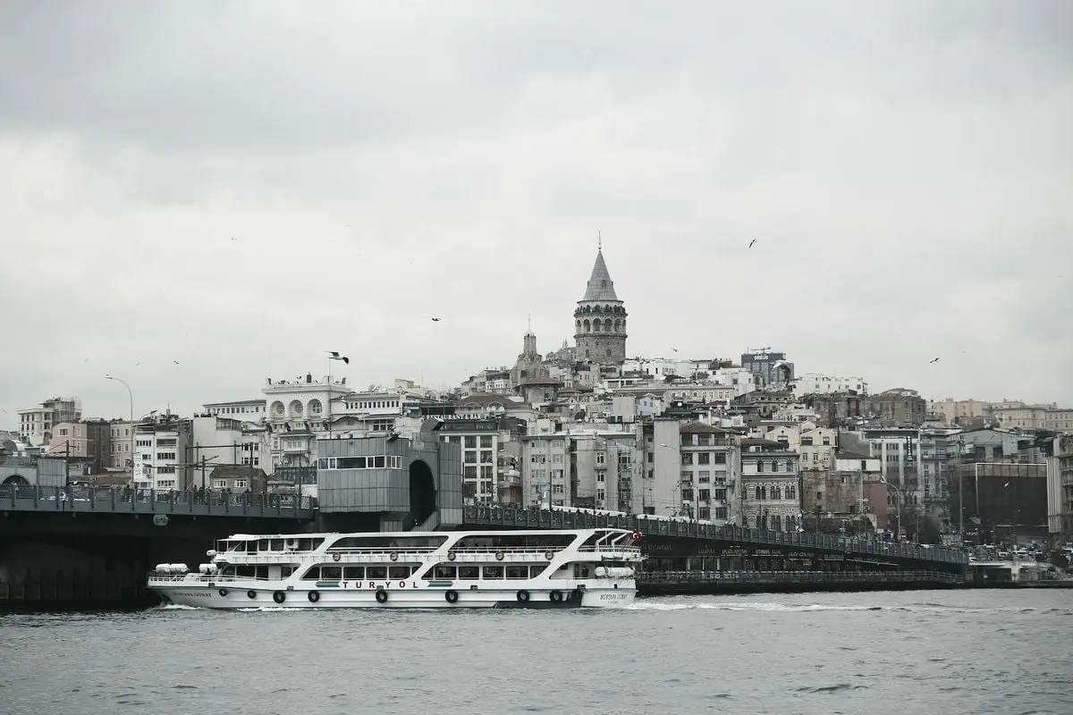 View of Galata Tower and Galata Bridge over the Bosphorus in Istanbul, Turkey, with a ferry passing by.