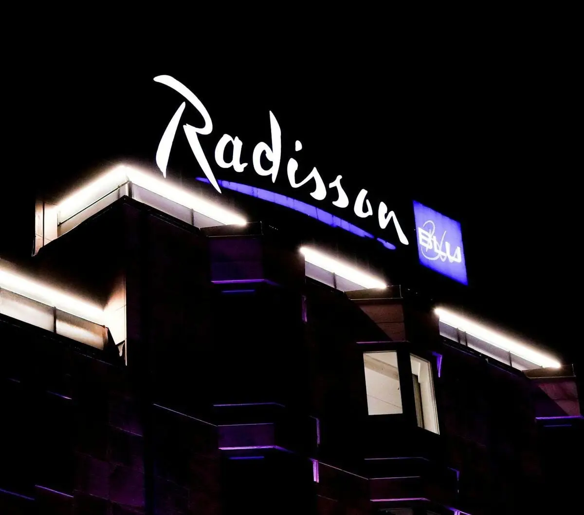 Illuminated Radisson Blu hotel building with neon signage captured at night.