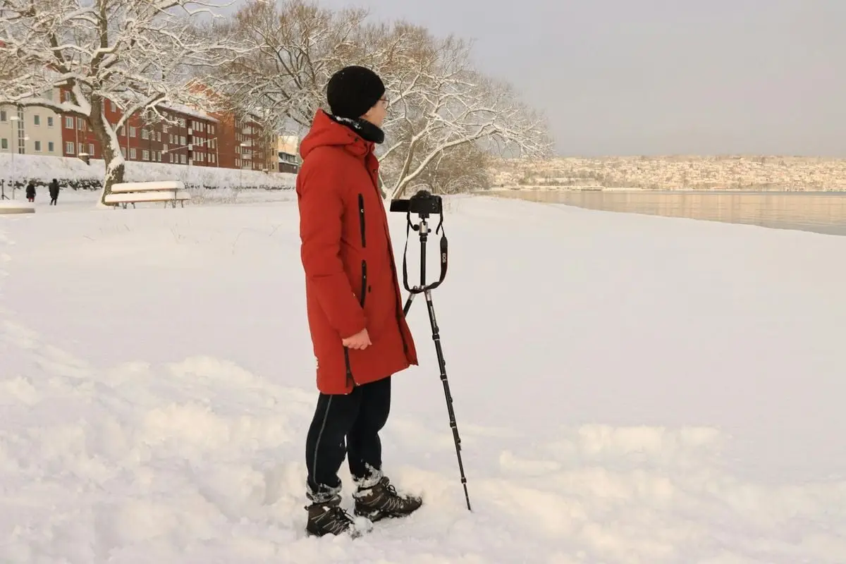Photographer in red coat with tripod capturing winter scene by snowy lake in Jönköping.