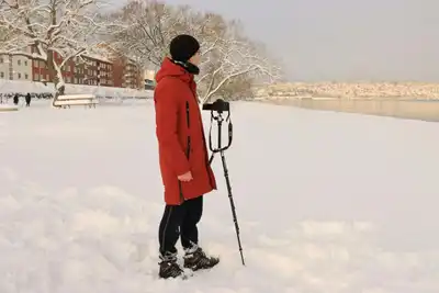 Photographer in red coat with tripod capturing winter scene by snowy lake in Jönköping.