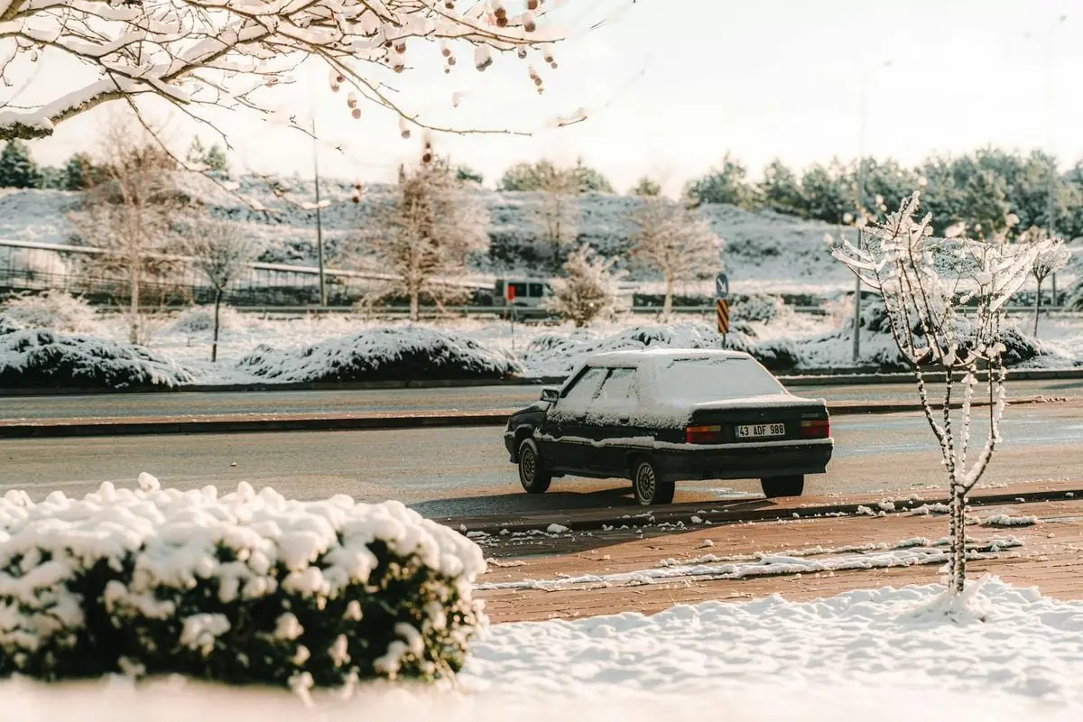 A vintage car covered in snow is parked in a winter countryside setting, showcasing a serene rural landscape.