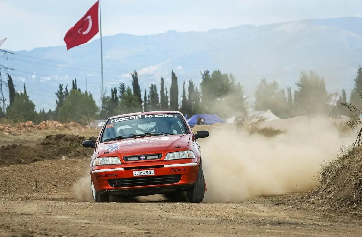 Fiat car engaging in a thrilling rallycross event on a dusty track in Turkey, with a prominent red flag in the background.