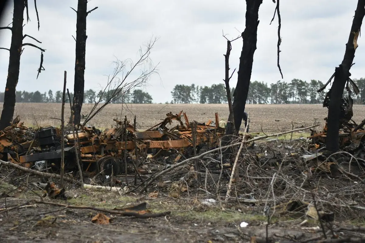 A rural field showcasing destroyed machinery and burnt trees, reflecting aftermath of destruction.