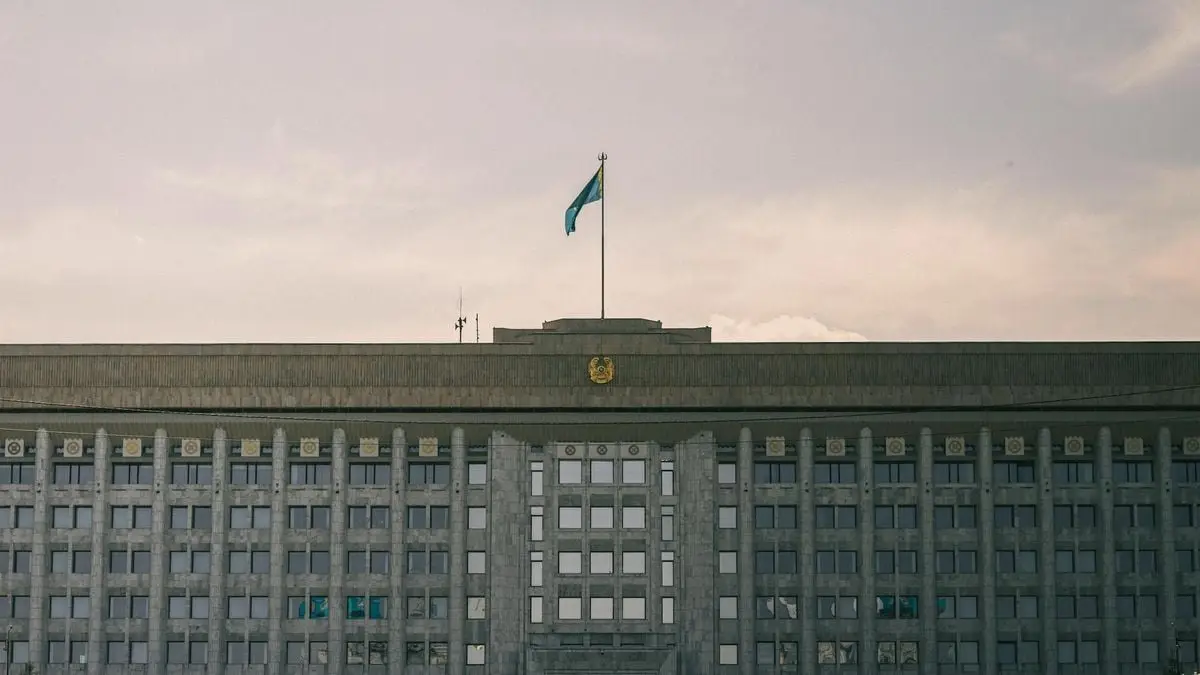 A grand government building with Kazakhstan flag in a clear sky.