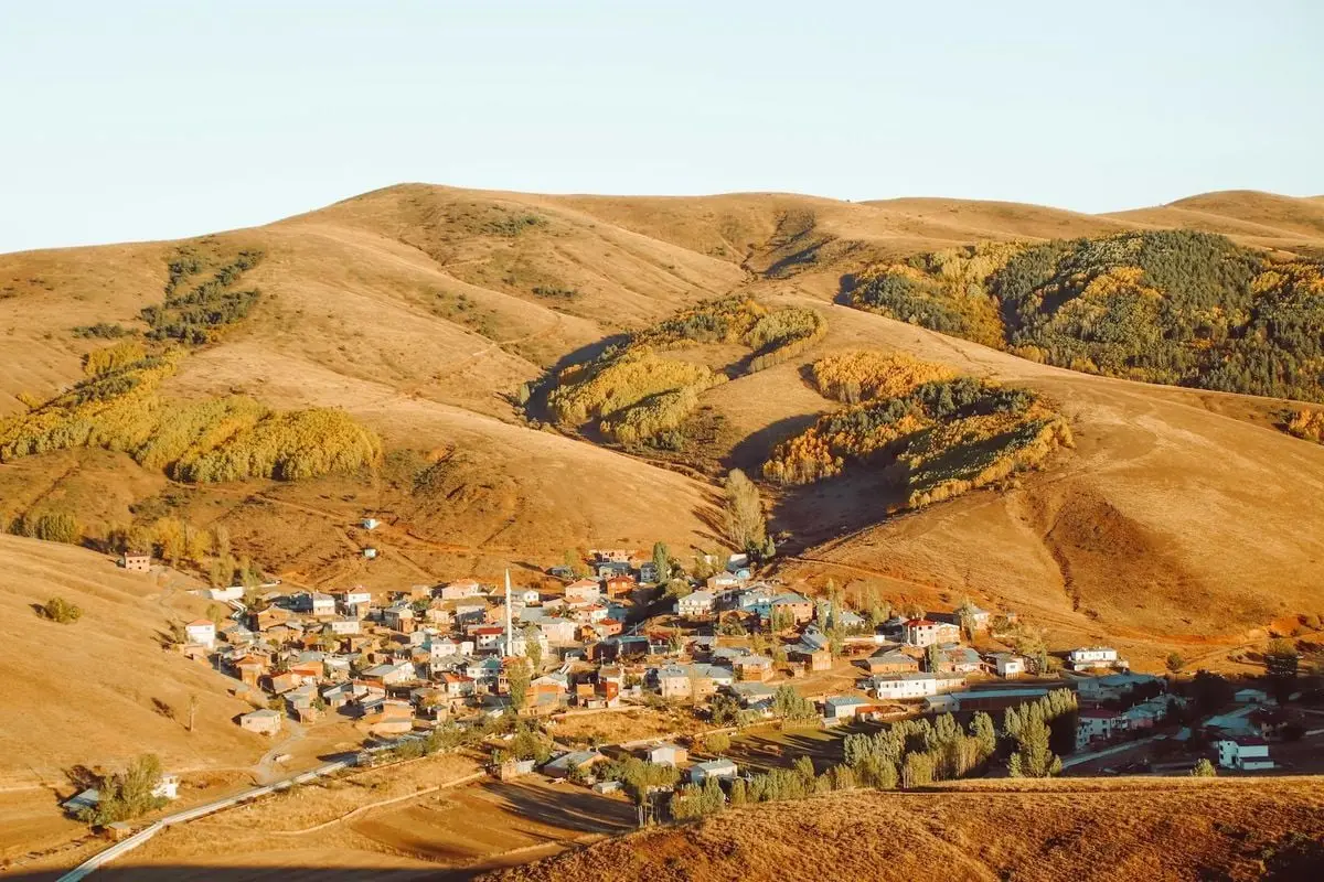 A serene aerial view of a small town nestled in rolling hills, bathed in warm sunlight.