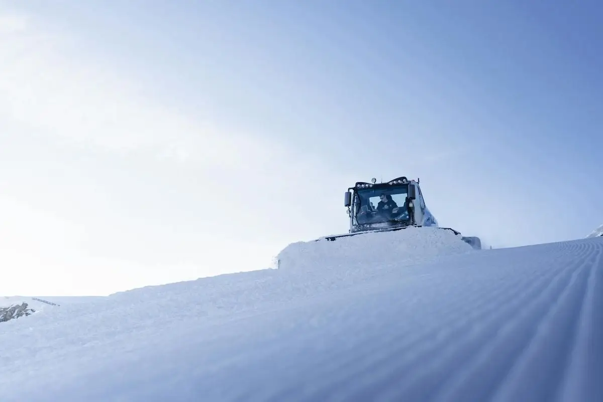 Snow groomer smoothing a ski slope under a clear blue sky in winter