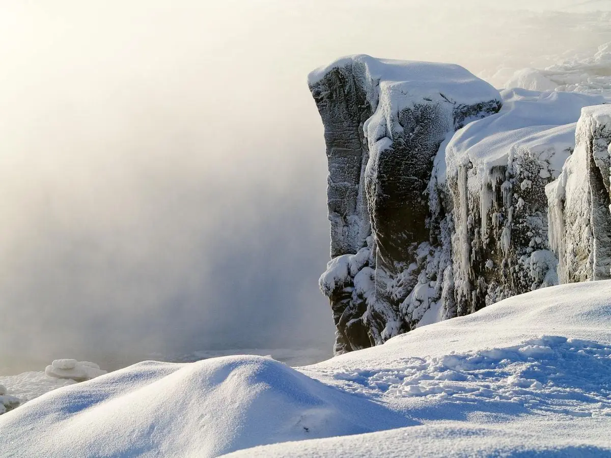 A dramatic frozen cliff covered in snow and icicles during winter, offering a serene and cold atmosphere.