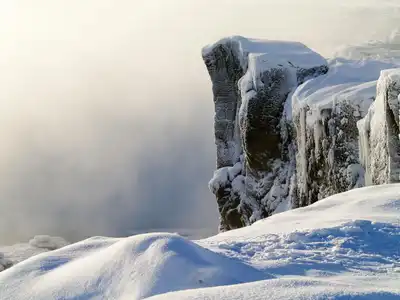A dramatic frozen cliff covered in snow and icicles during winter, offering a serene and cold atmosphere.