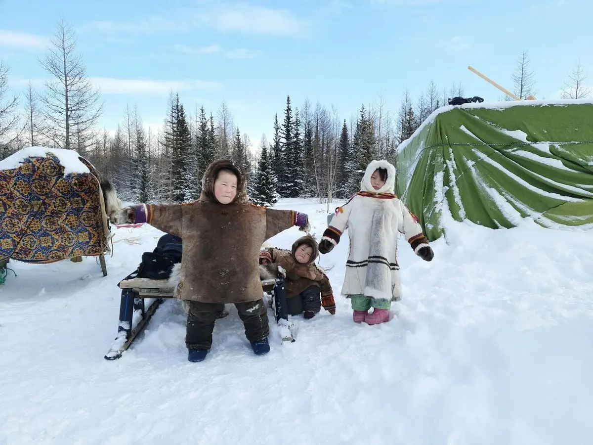 Three children dressed in traditional warm clothing enjoy their time in a snowy outdoor setting.