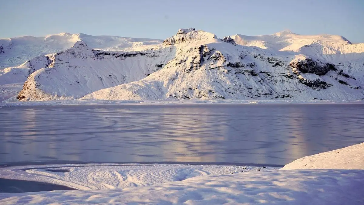 A stunning panorama of a snow-covered mountain and frozen lake under soft sunlight.