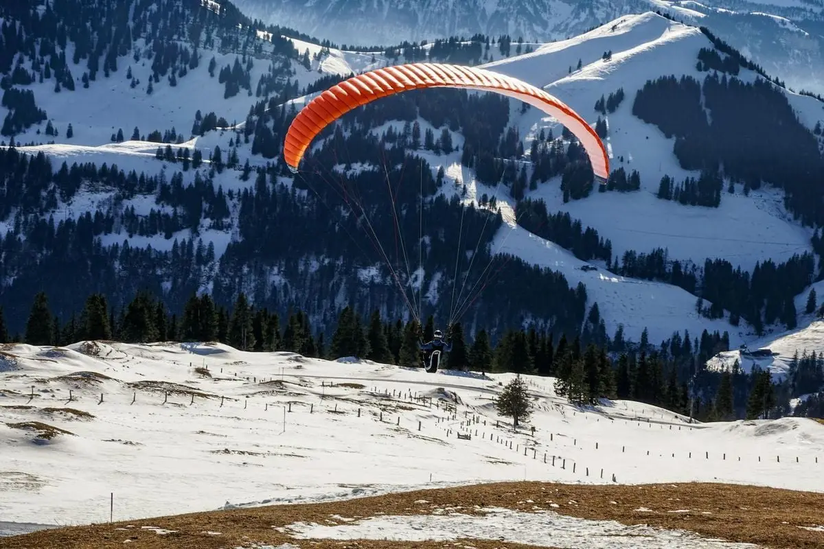 A paraglider soars over a snow-covered mountain landscape during winter.