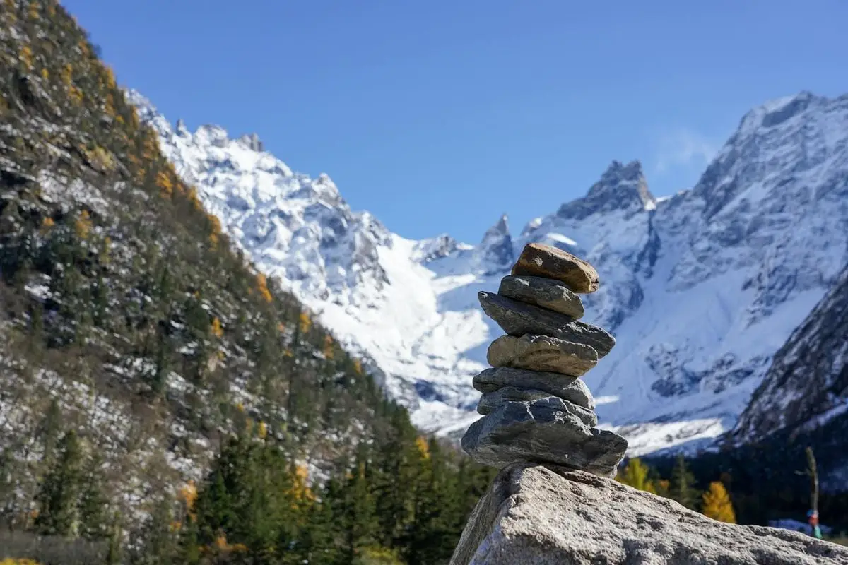 A tranquil mountain scene with stacked rocks and snow-capped peaks under a clear blue sky.