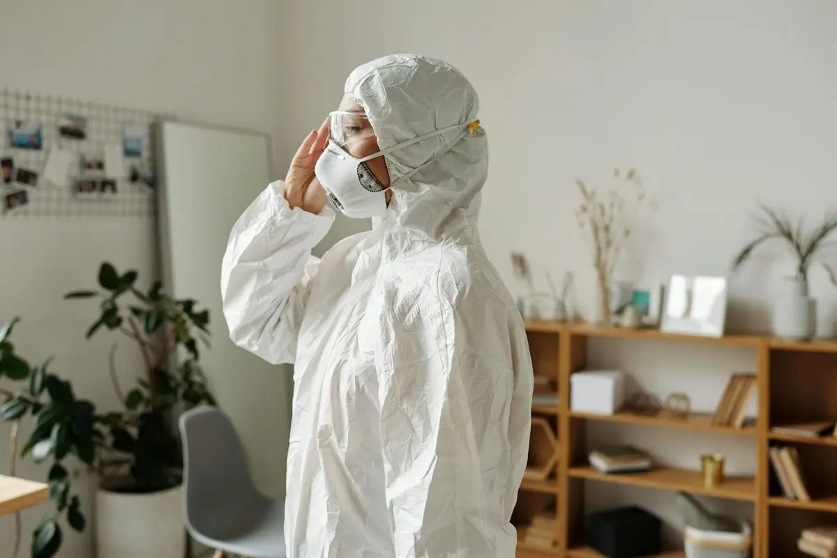Healthcare worker wearing full protective gear including a mask, goggles, and suit, inside a room.