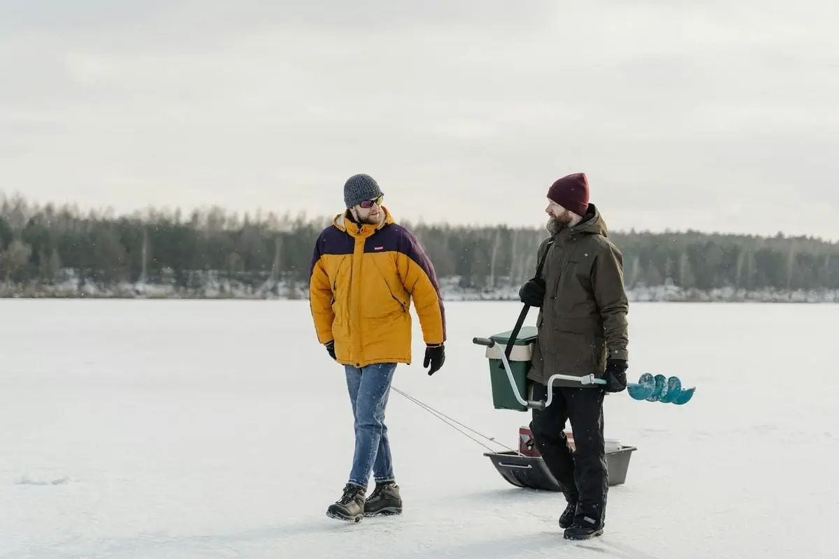Two men in winter clothing engaging in ice fishing on a frozen lake, enjoying a cold winter day outdoors.