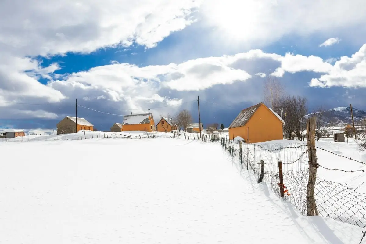 Snowy landscape with orange houses and fence under a clear blue sky in winter.