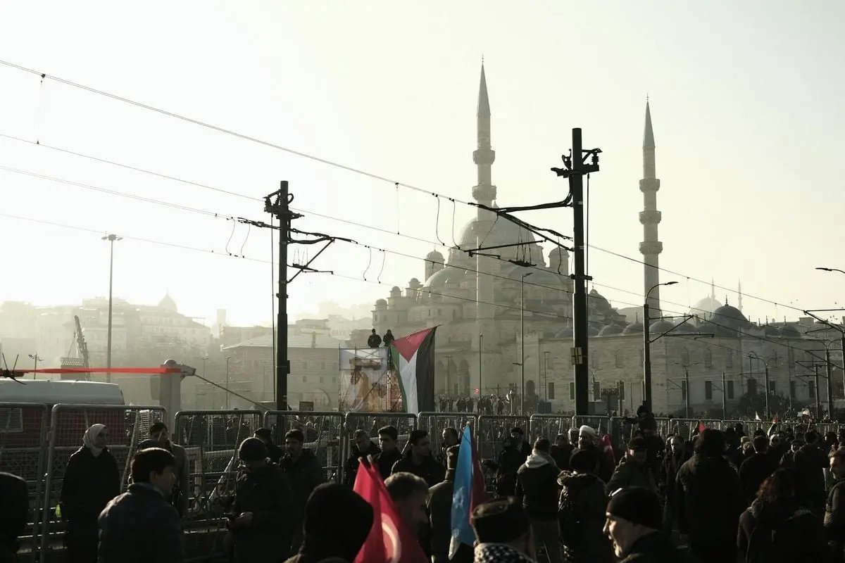 A bustling crowd gathers near the iconic Sultan Ahmed Mosque in Istanbul during dusk, creating a dynamic urban scene.