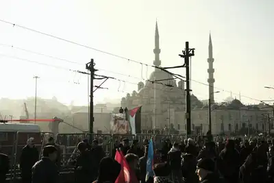 A bustling crowd gathers near the iconic Sultan Ahmed Mosque in Istanbul during dusk, creating a dynamic urban scene.