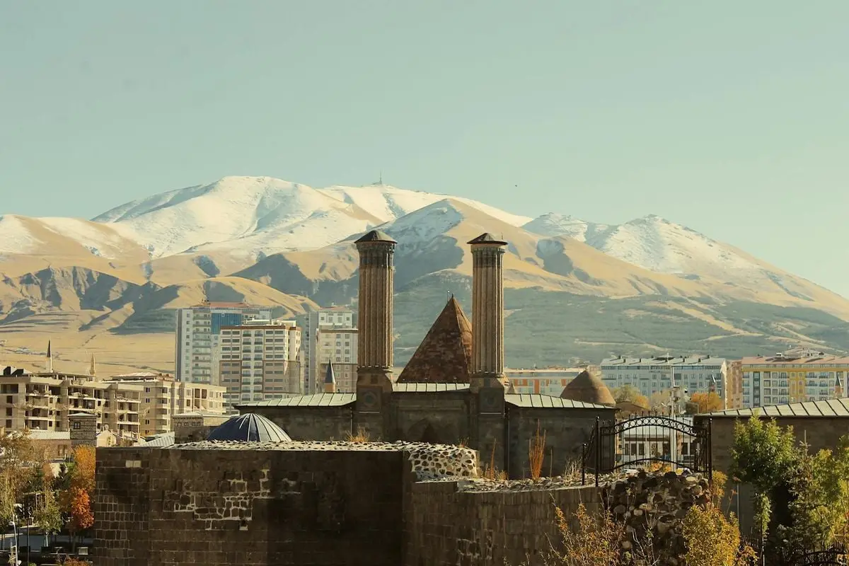 The historic Cifte Minareli Medrese with snow-covered mountains in Erzurum, Turkey.