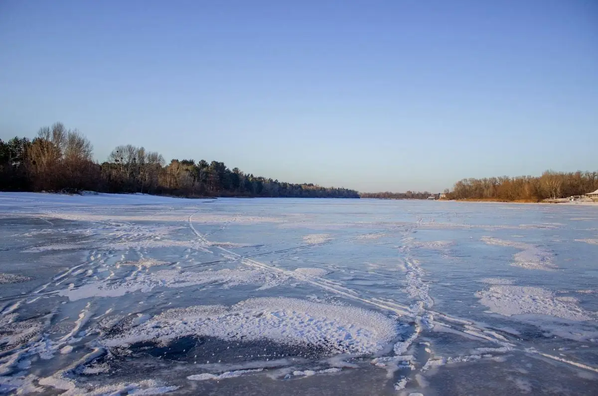Serene frozen river landscape on a bright winter day with a clear blue sky.