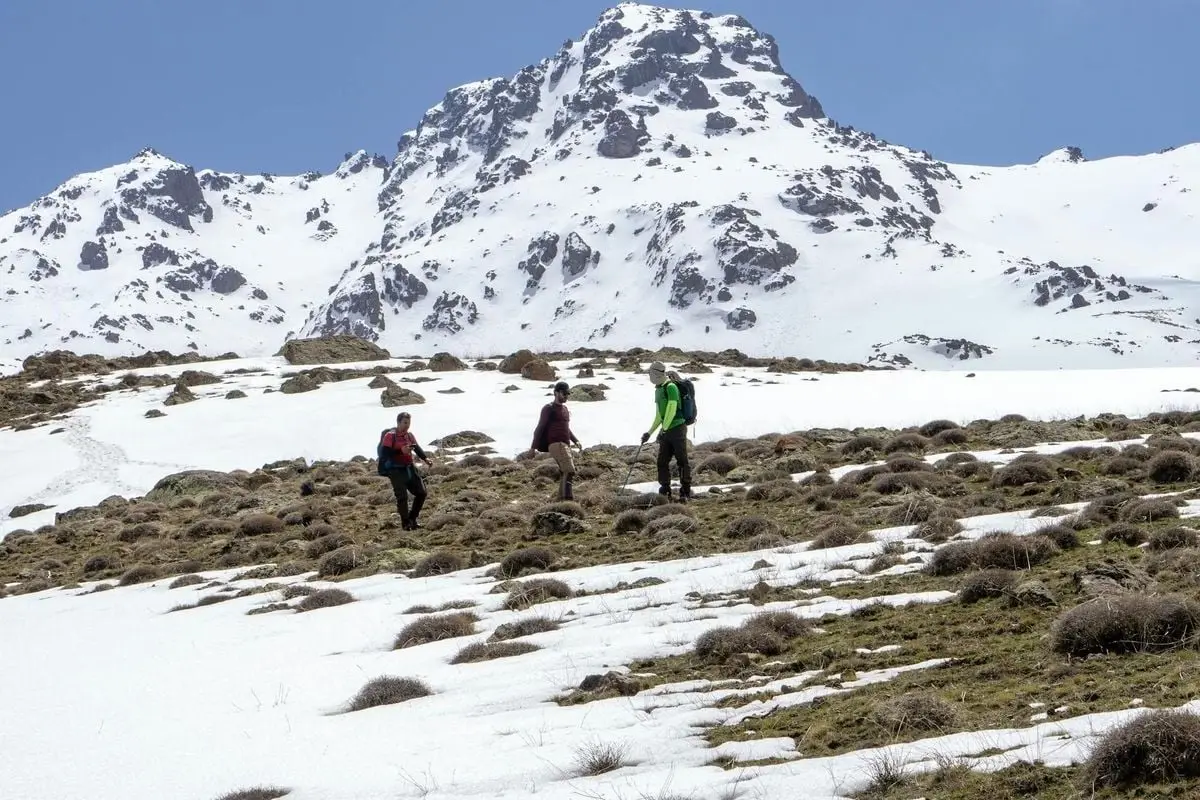 Hikers trekking through snow-covered mountains in Van, Turkey, under clear blue skies.