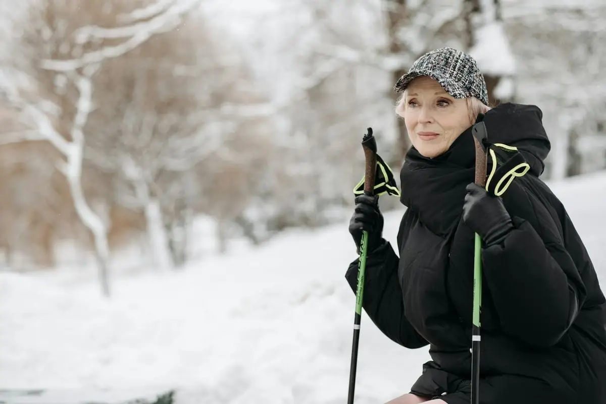 Senior woman enjoying a winter hike with trekking poles in a snowy landscape.
