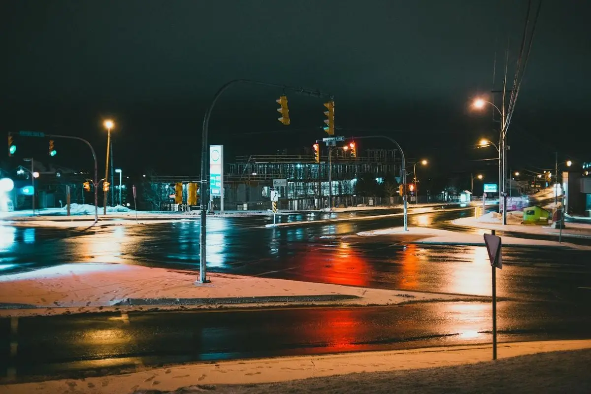 Wet asphalt roadways with streetlamps and traffic lights against buildings under dark sky in evening town
