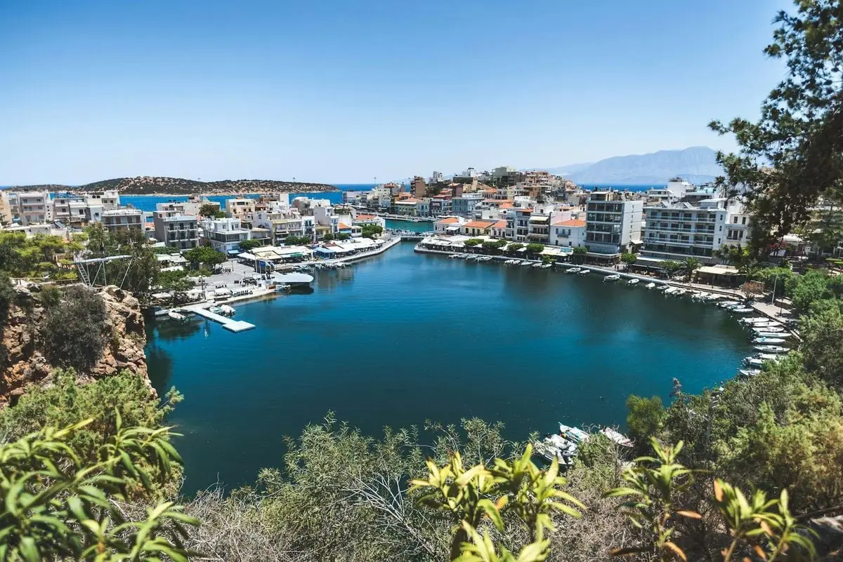 Picturesque harbor in Agios Nikolaos, Crete surrounded by urban architecture and clear blue waters.
