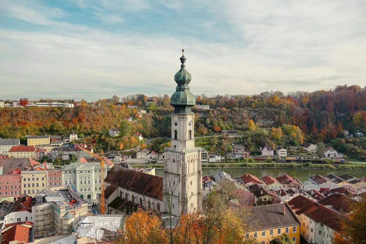 Panoramic view of an old church tower amidst vibrant autumn foliage in a European town.