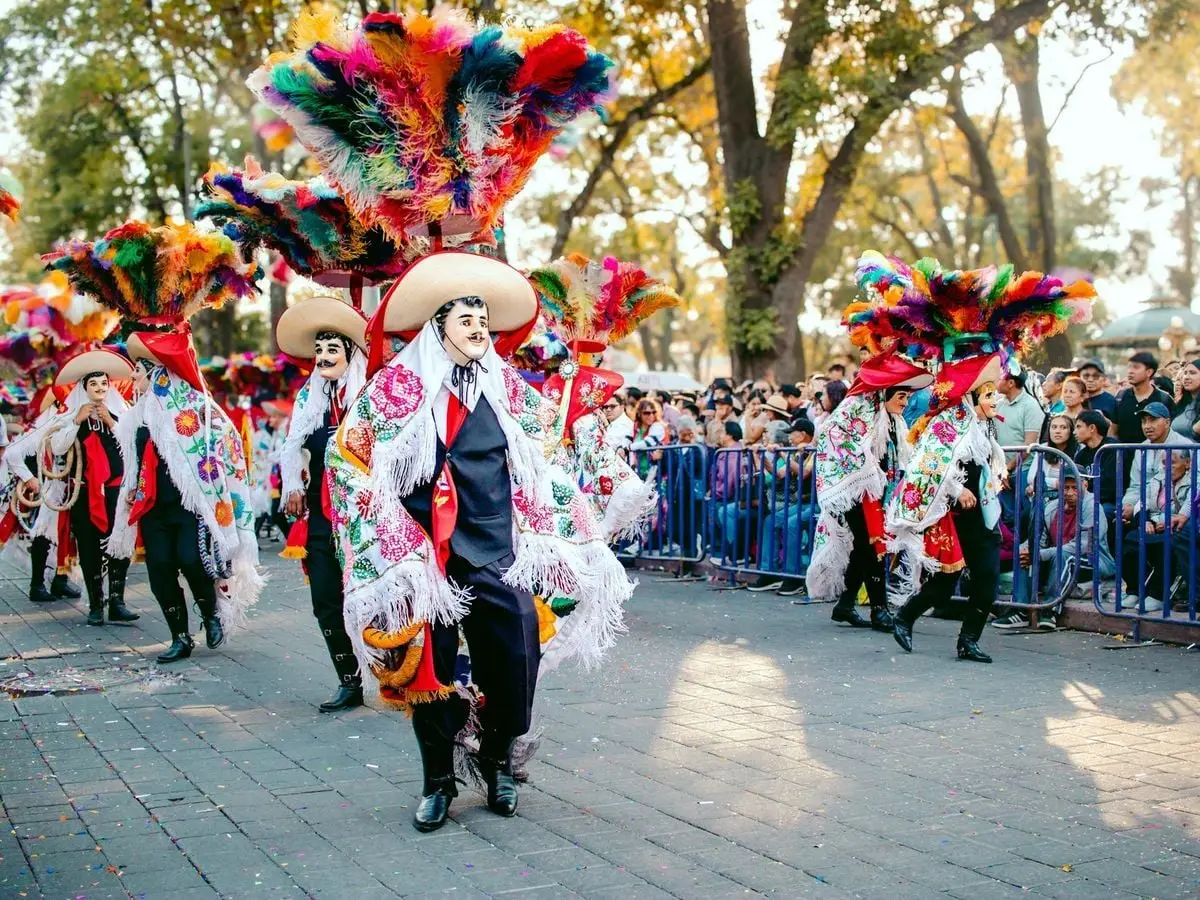 Colorful festival parade featuring traditional costumes and feathered hats, attracting a lively crowd.