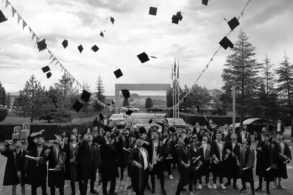 A group of university graduates in gowns and caps celebrate outdoors by tossing their caps into the air.