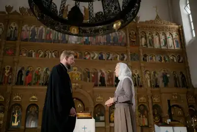 A priest and a parishioner engage in conversation inside an ornate Orthodox church.