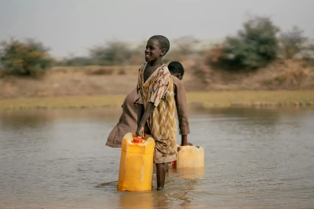 Smiling children collecting water from a river in rural area.