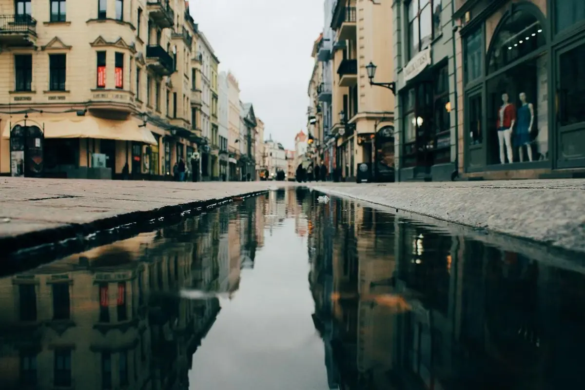 Capture of a Toruń street with reflections on wet pavement, showcasing historic architecture.