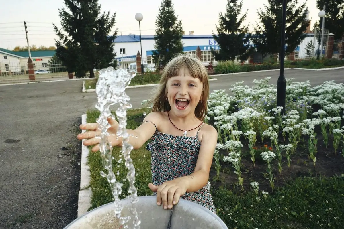 A happy young girl enjoying a summer day playing with a water fountain in a park.