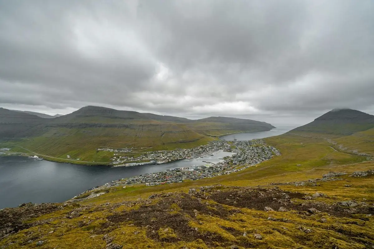 A breathtaking view of a coastal town nestled between dramatic mountains under a cloudy sky.