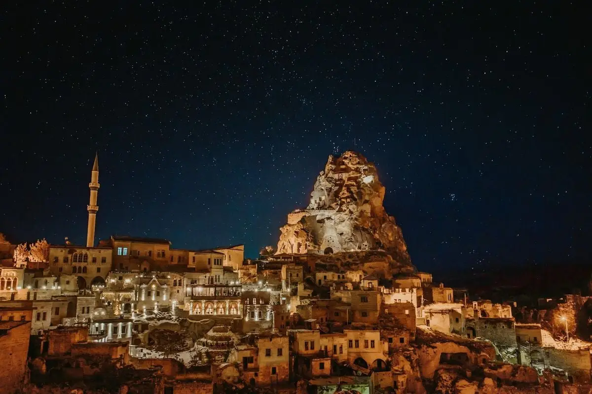Stunning starry night view of Cappadocia, Türkiye, highlighting illuminated cave dwellings and rock formations.