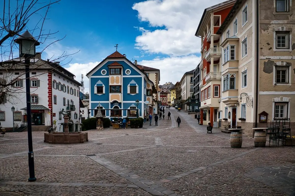 Vibrant town square in Sankt Ulrich, Trentino-Südtirol, showcasing colorful buildings and cobblestone paths.