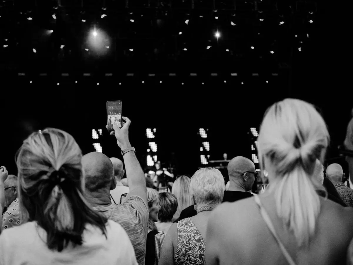 Black and white photo of a concert audience capturing memories with a smartphone.