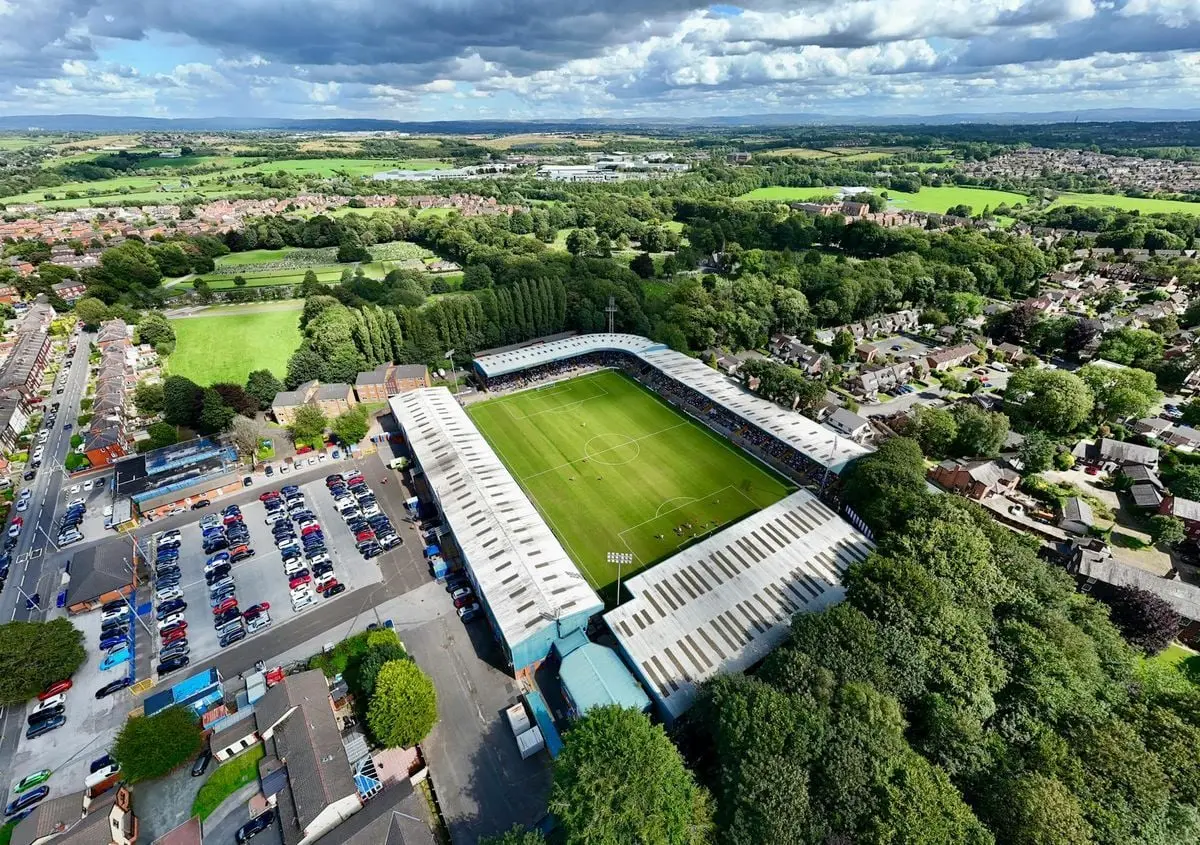 Drone shot capturing Gigg Lane Stadium, surrounded by lush greenery in Bury, England.